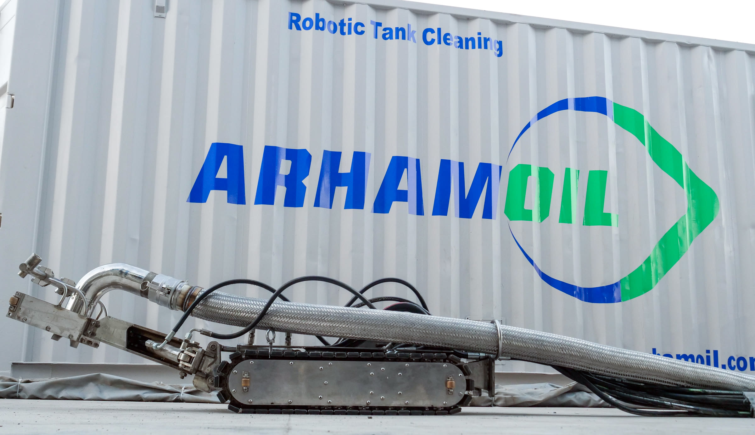 Arham Oil tracked tank-cleaning robot in front of a branded Robotic Tank Cleaning container.